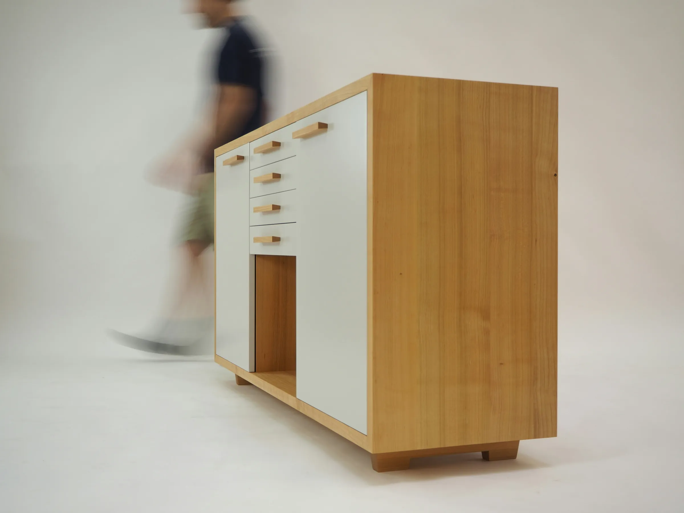 Oak and white sideboard on a studio floor as a person walks past