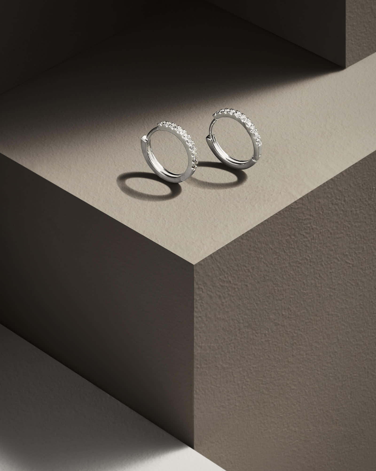 Two simple silver rings resting on a neutral-toned, geometric pedestal with soft shadows.