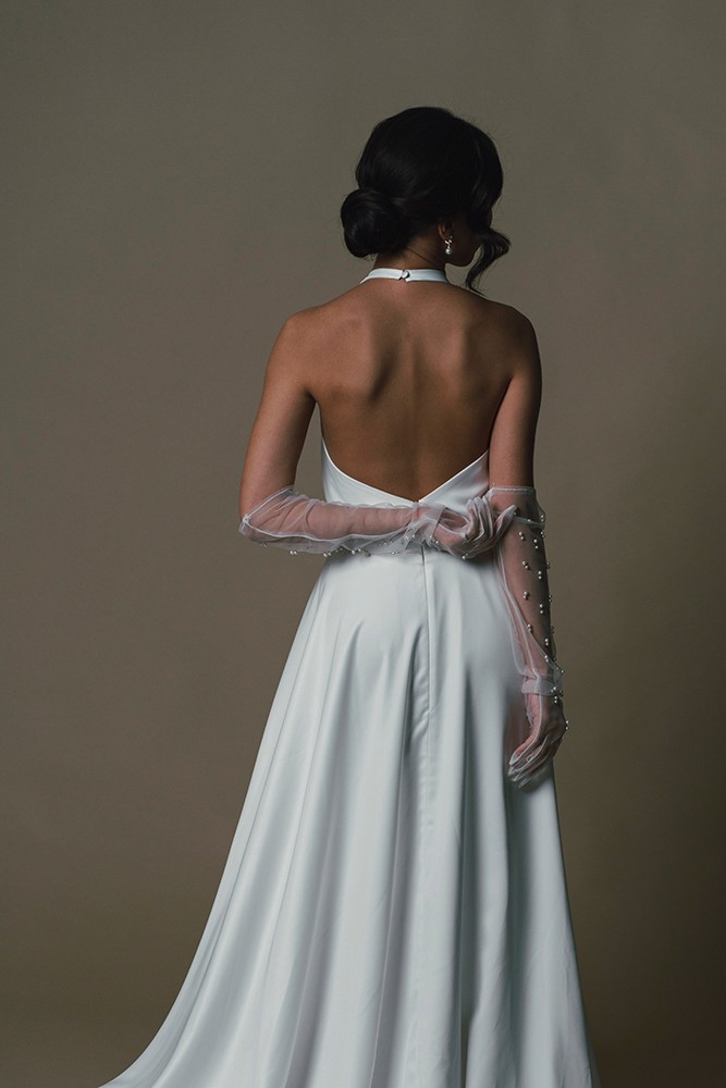 Bride photographed from behind in an open low-back gown against a dark backdrop, fine art bridal editorial by Eva Sitko