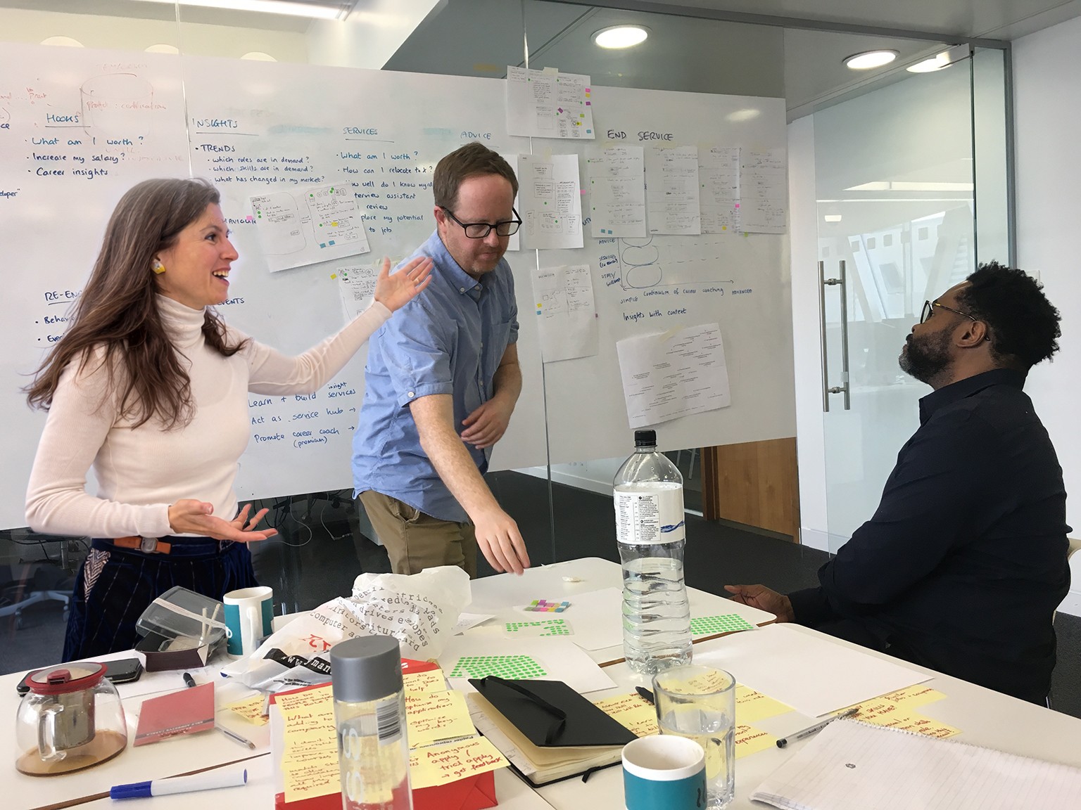 3 people workshoping in an office with a lot of post it's on the wall