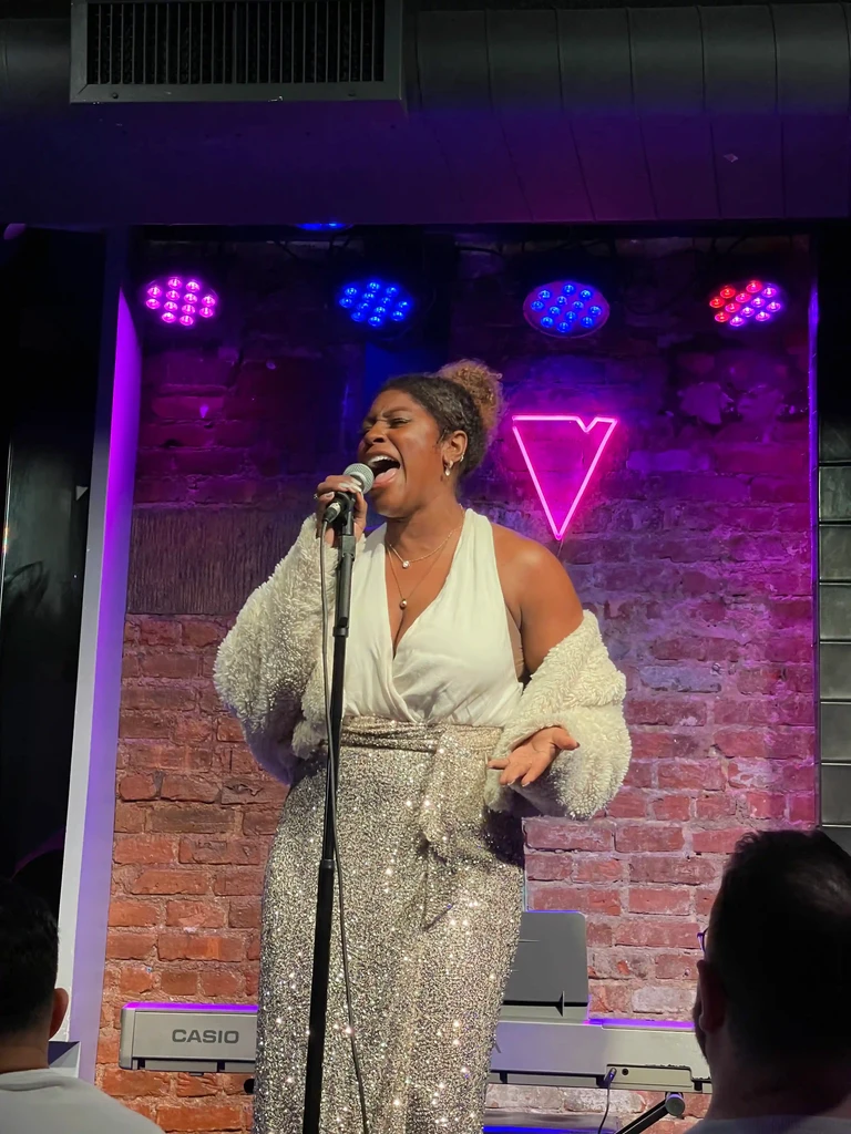 A performer holds a note at the microphone, lit in magenta