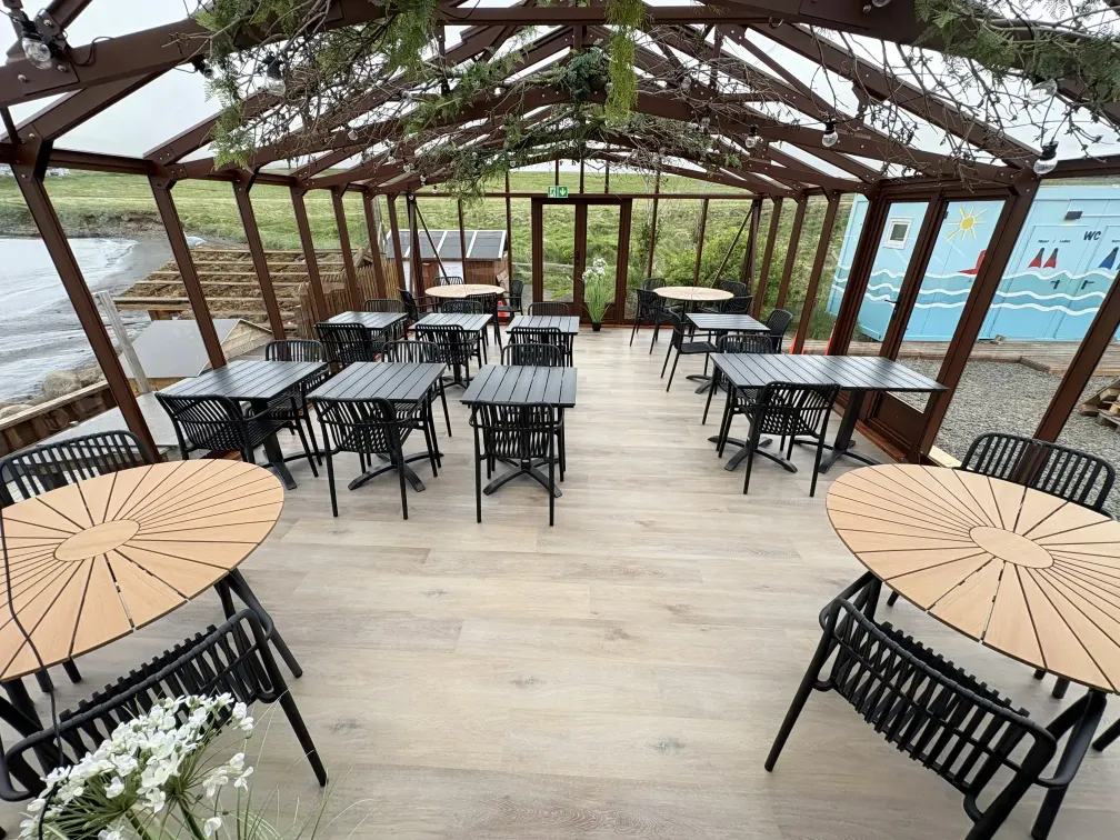 Coffee drinks and light meals served on a wooden board at an outdoor beachside cafe table.