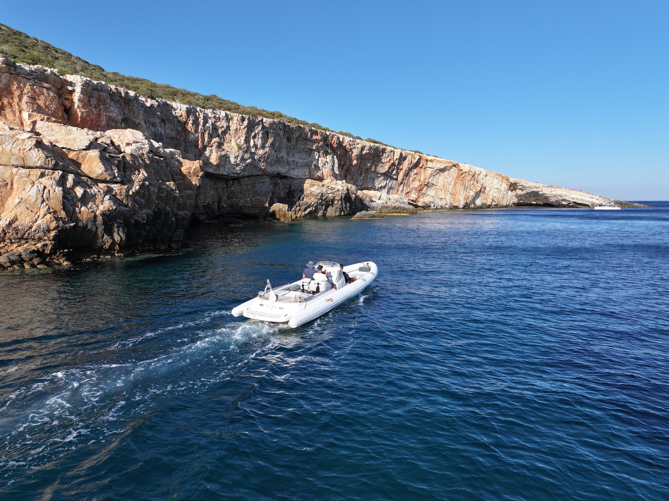 White Airship 30 yacht cruising in deep blue waters near dramatic limestone cliffs and sea caves in the Cyclades.