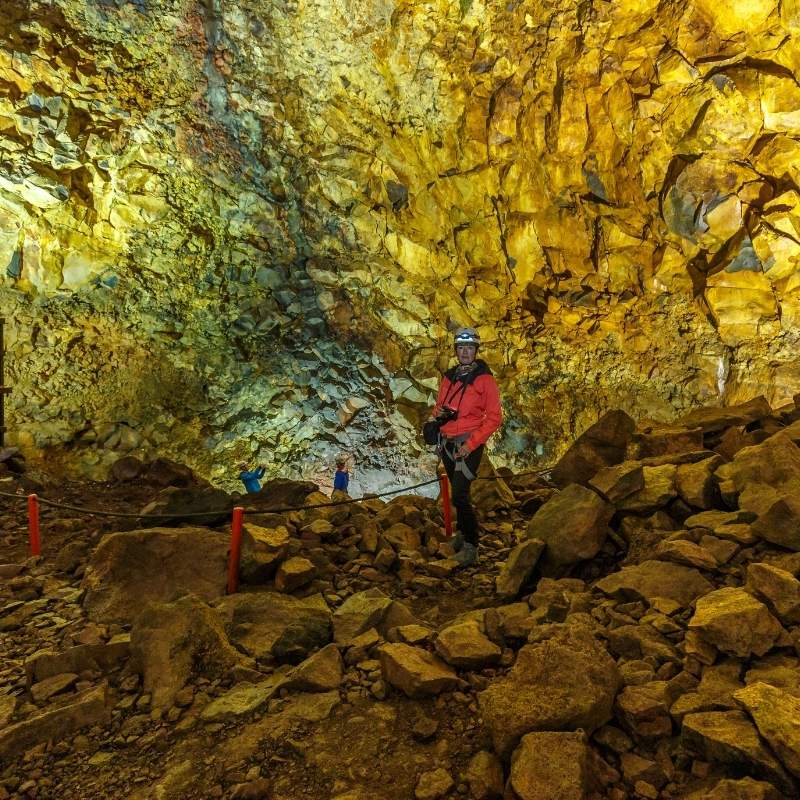 Person standing inside the Þríhnjúkagígar magma chamber in Iceland, surrounded by towering, multicolored rock walls formed by ancient volcanic activity.