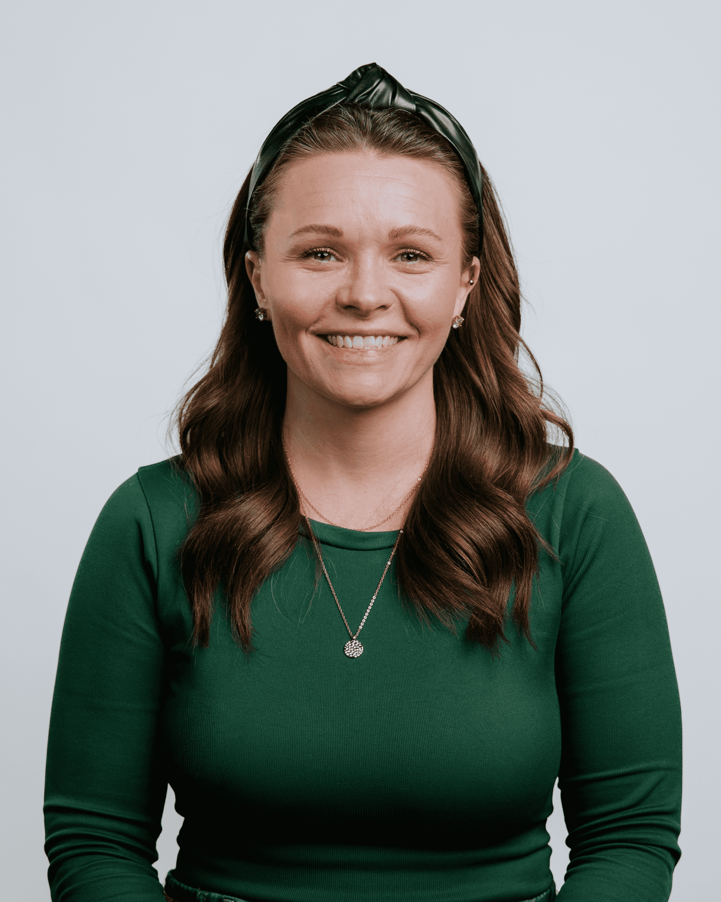 A smiling woman with long brown hair, wearing a brown top, against a plain white background.