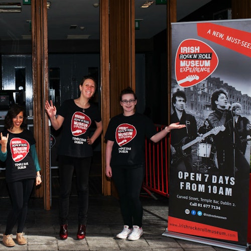 Three people in matching t-shirts standing next to a sign for the Irish Rock 'n' Roll Museum Experience.