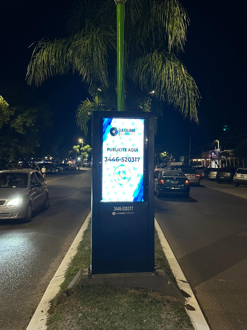 Tótem publicitario iluminado en avenida con tránsito nocturno