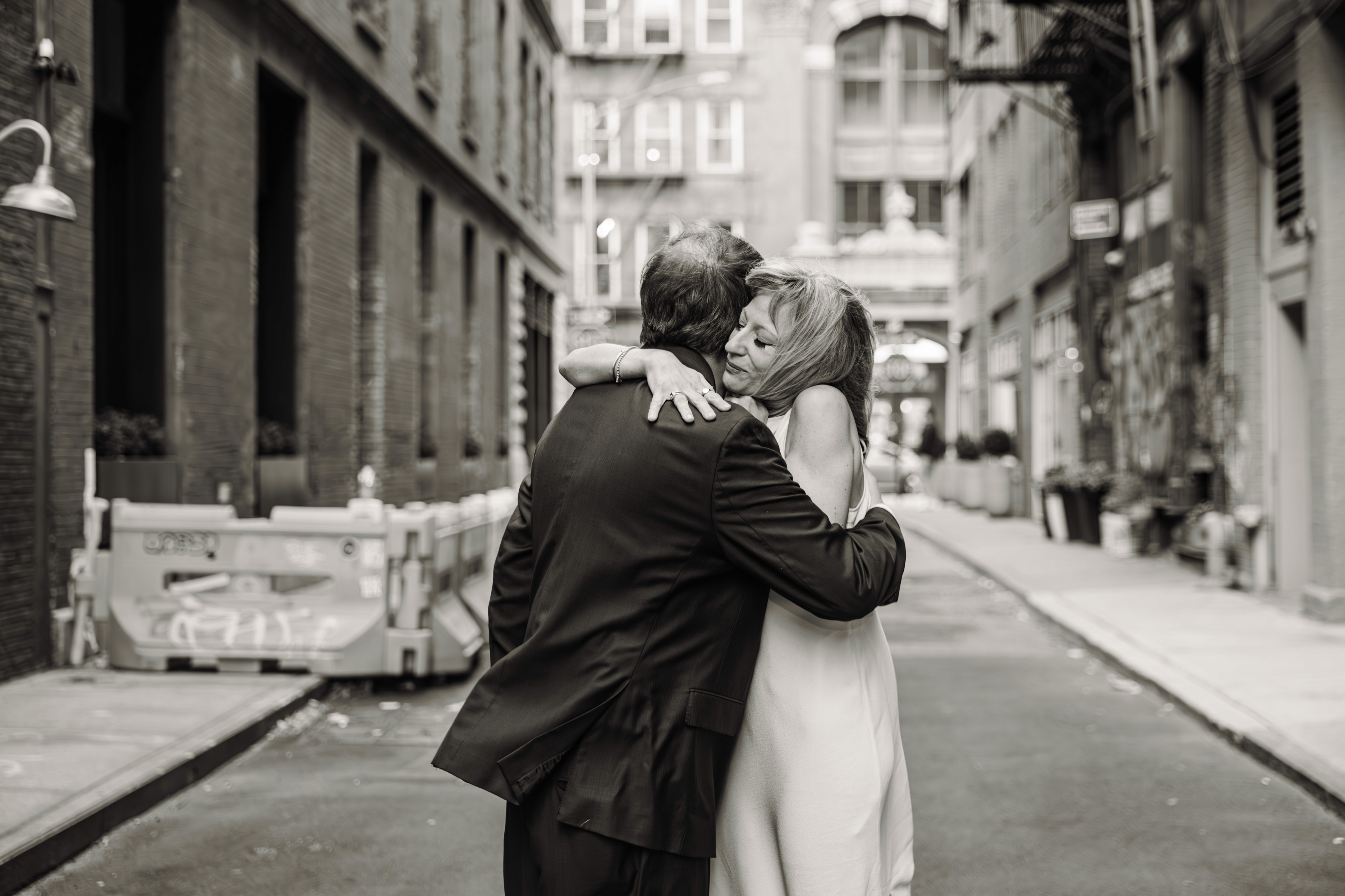 Couple sharing a tender embrace beneath the iconic Staple Street Bridge in Tribeca, NYC — moody black and white couples photography by Lizz Spano Photography, New York City couples photographer.