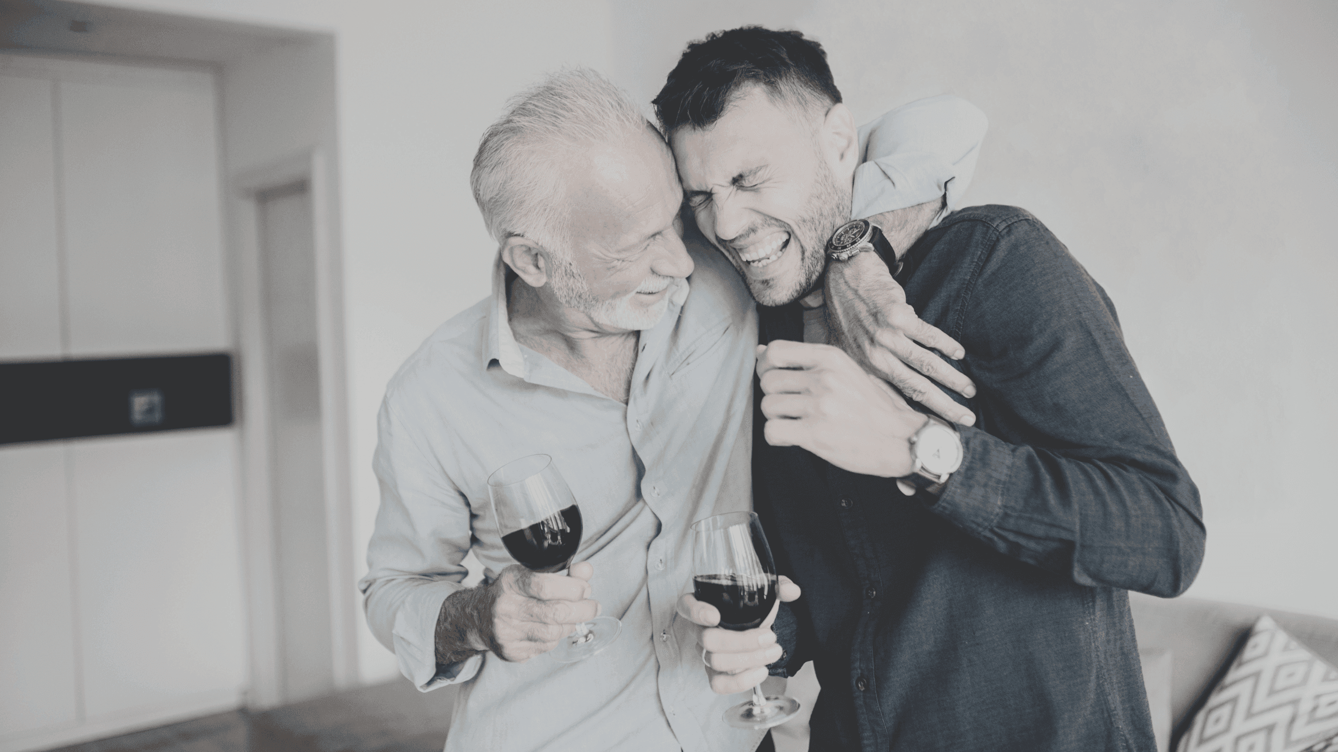 A photograph of two men laughing and hugging, each holding a glass of red wine