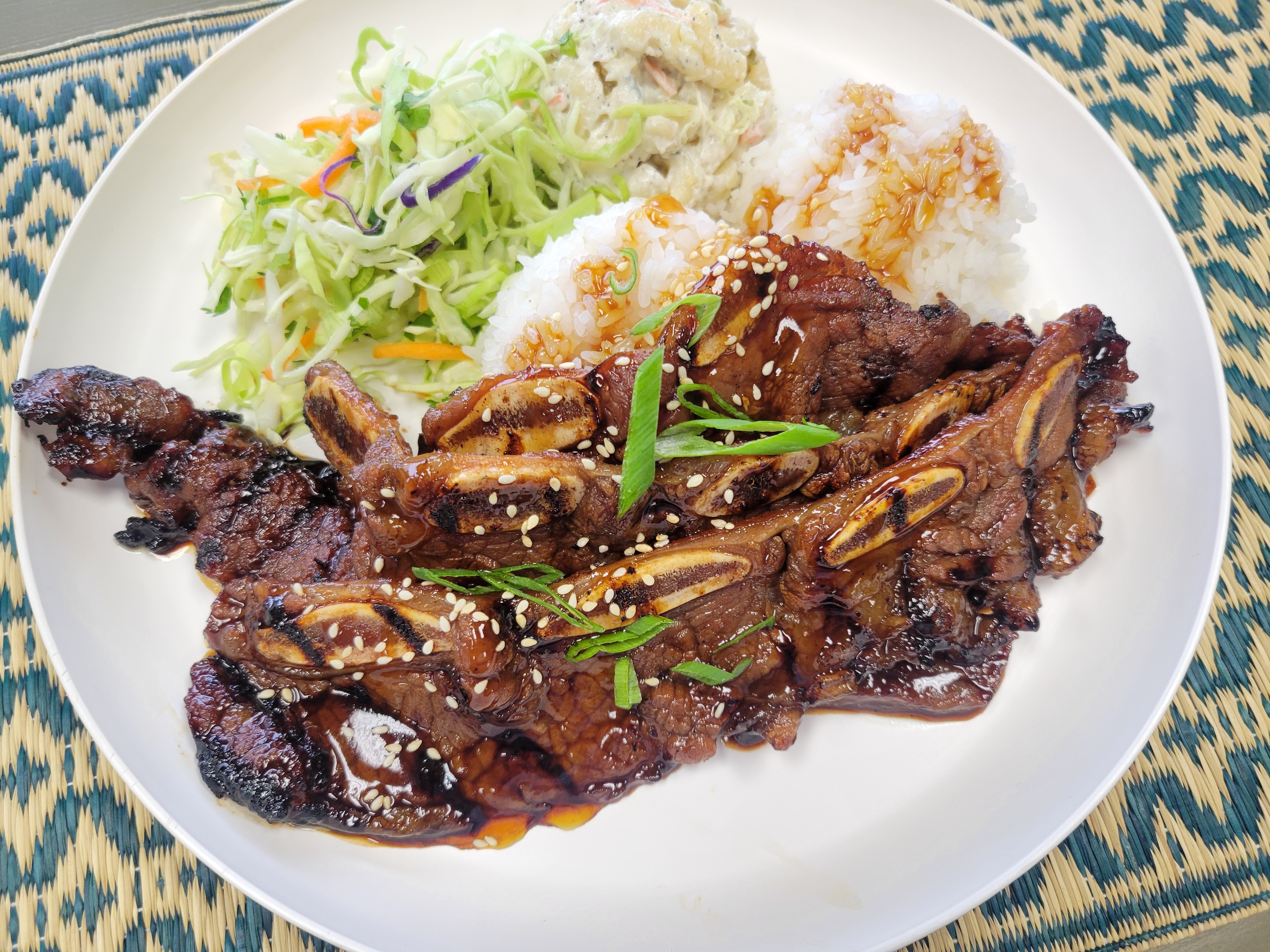 Generous serving of grilled Hawaiian Short Ribs with char marks, served over Jasmine rice with a side of creamy mac salad and Asian slaw.