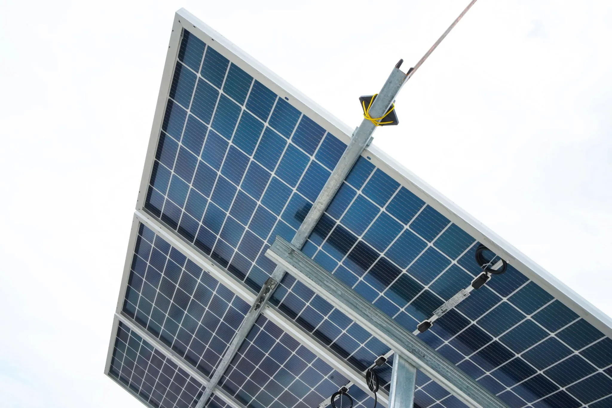Tilted solar panel on a steel mount seen from below against a clear sky