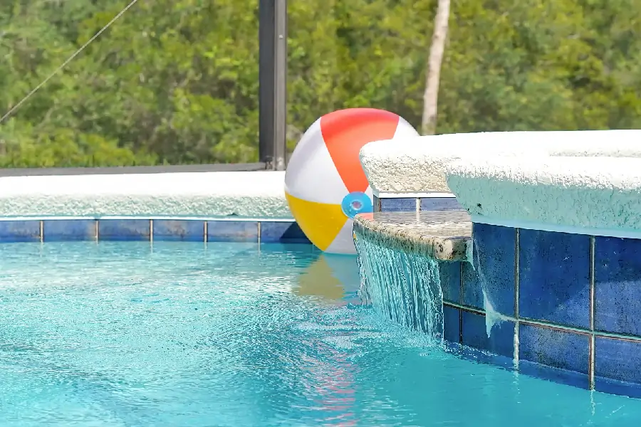 A colorful beach ball floats in a swimming pool against a backdrop of a blue tiled wall.