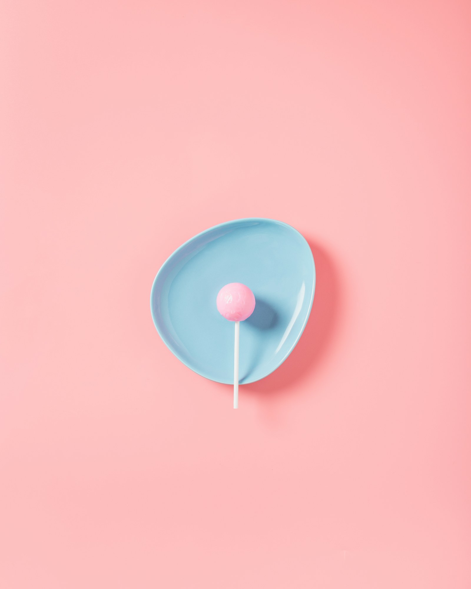 A pink lollipop on a pale blue plate against a pink wall