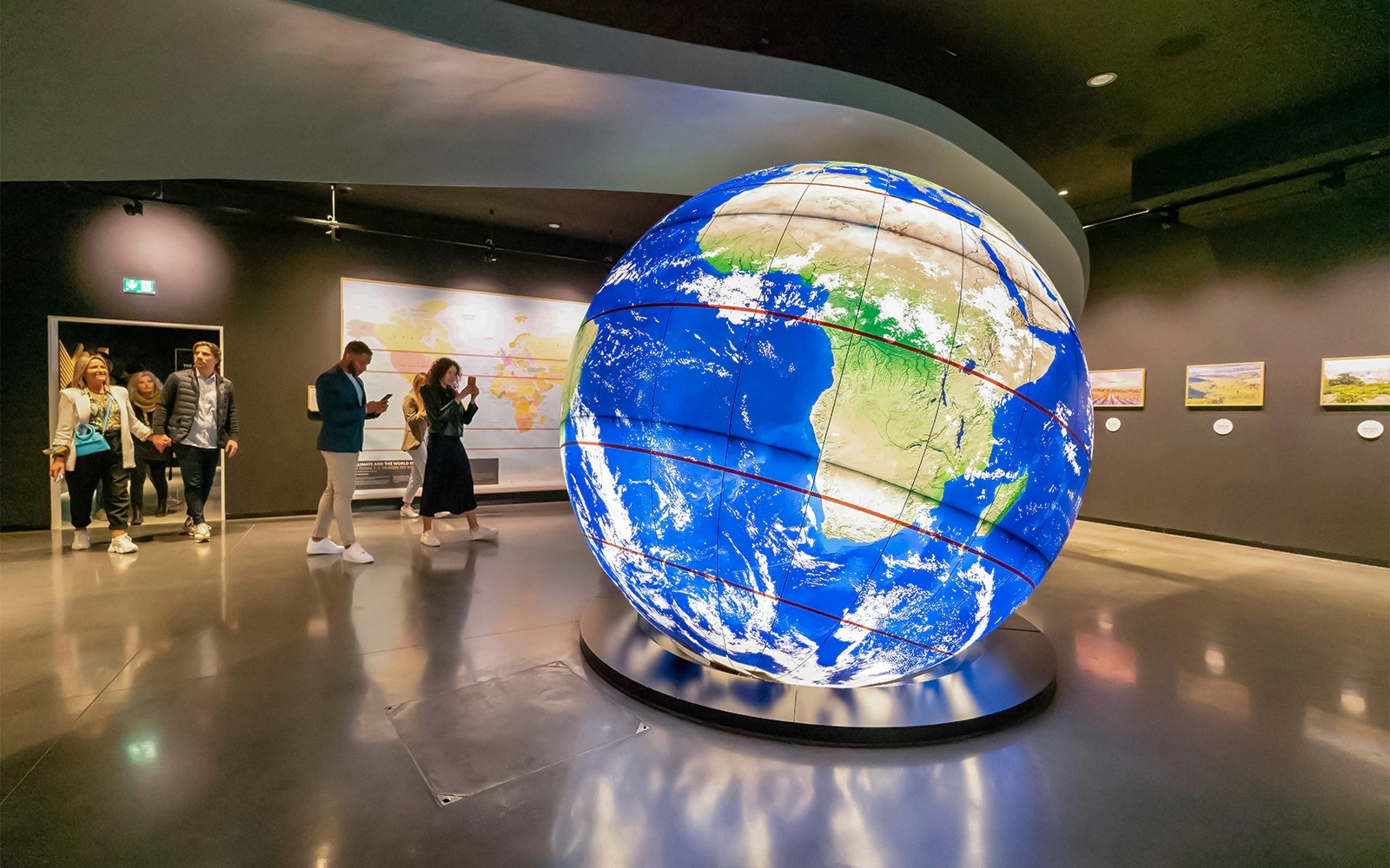 Látogatók, akik egy nagy, megvilágított földgömböt fedeznek fel a The Wine Experience kiállításon.