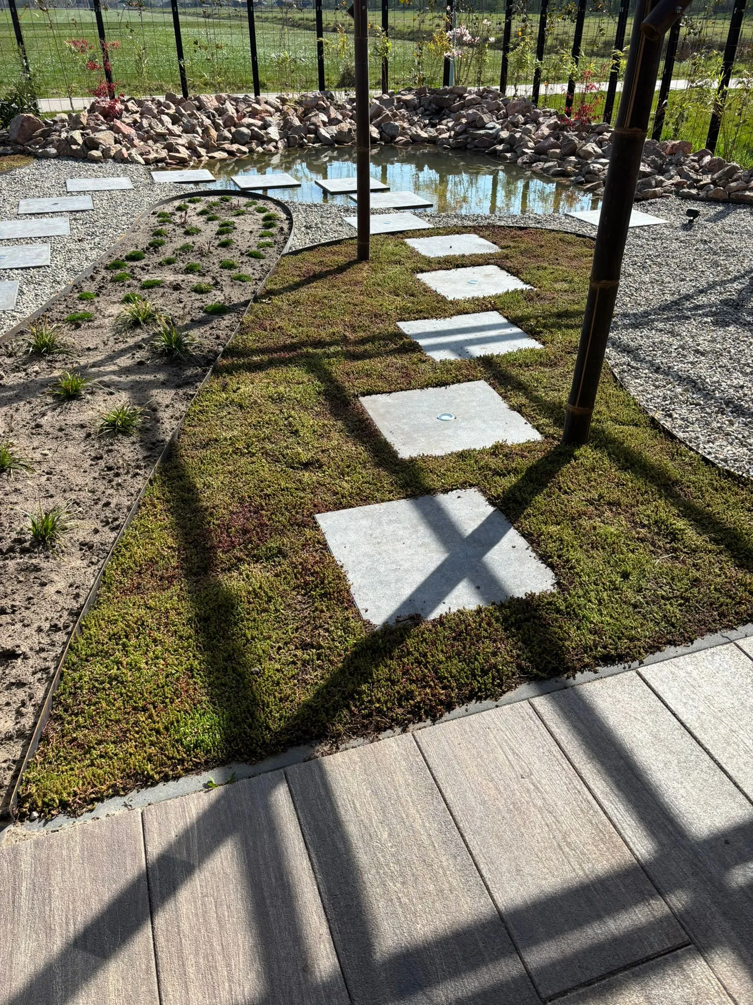 Japanse tuin met betonnen stapstenen in mos en grind, kleine beplanting en vijver met rotsen bij nieuwbouwwoning in Gorredijk.