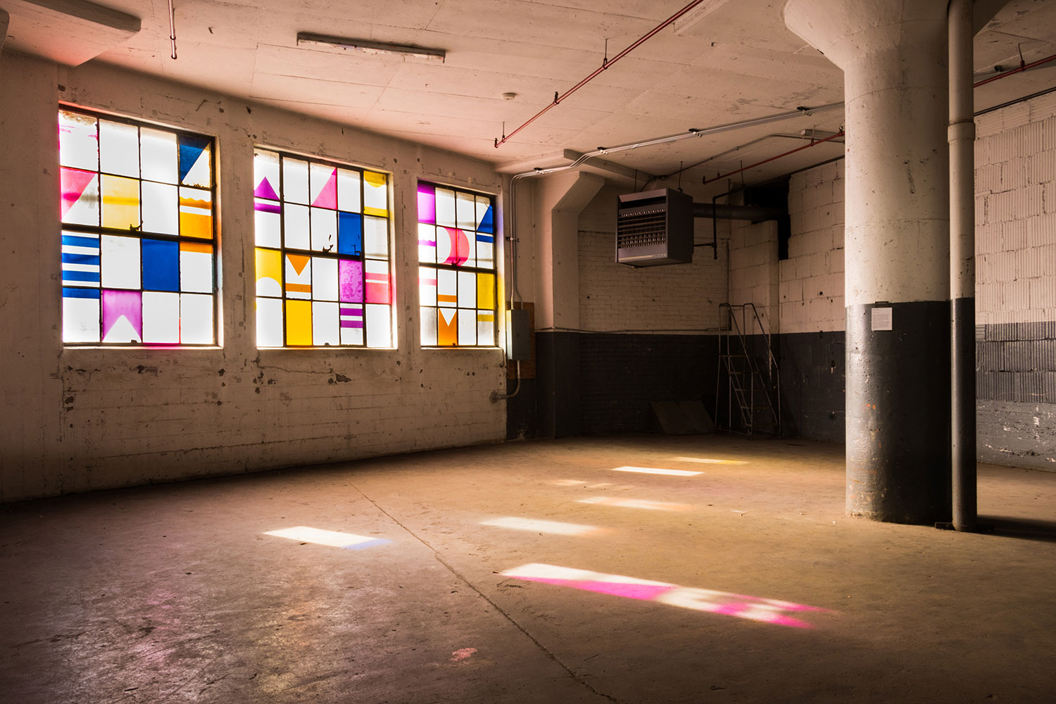 Shape/Shift mural is made of brightly colored cut acrylic installed in a set of large industrial windows