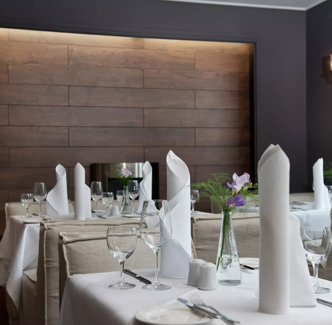 Ein eingedeckter Tisch im Restaurant mit Tischdecke, aufgestellten Servietten und einer kleinen Blume auf dem Tisch