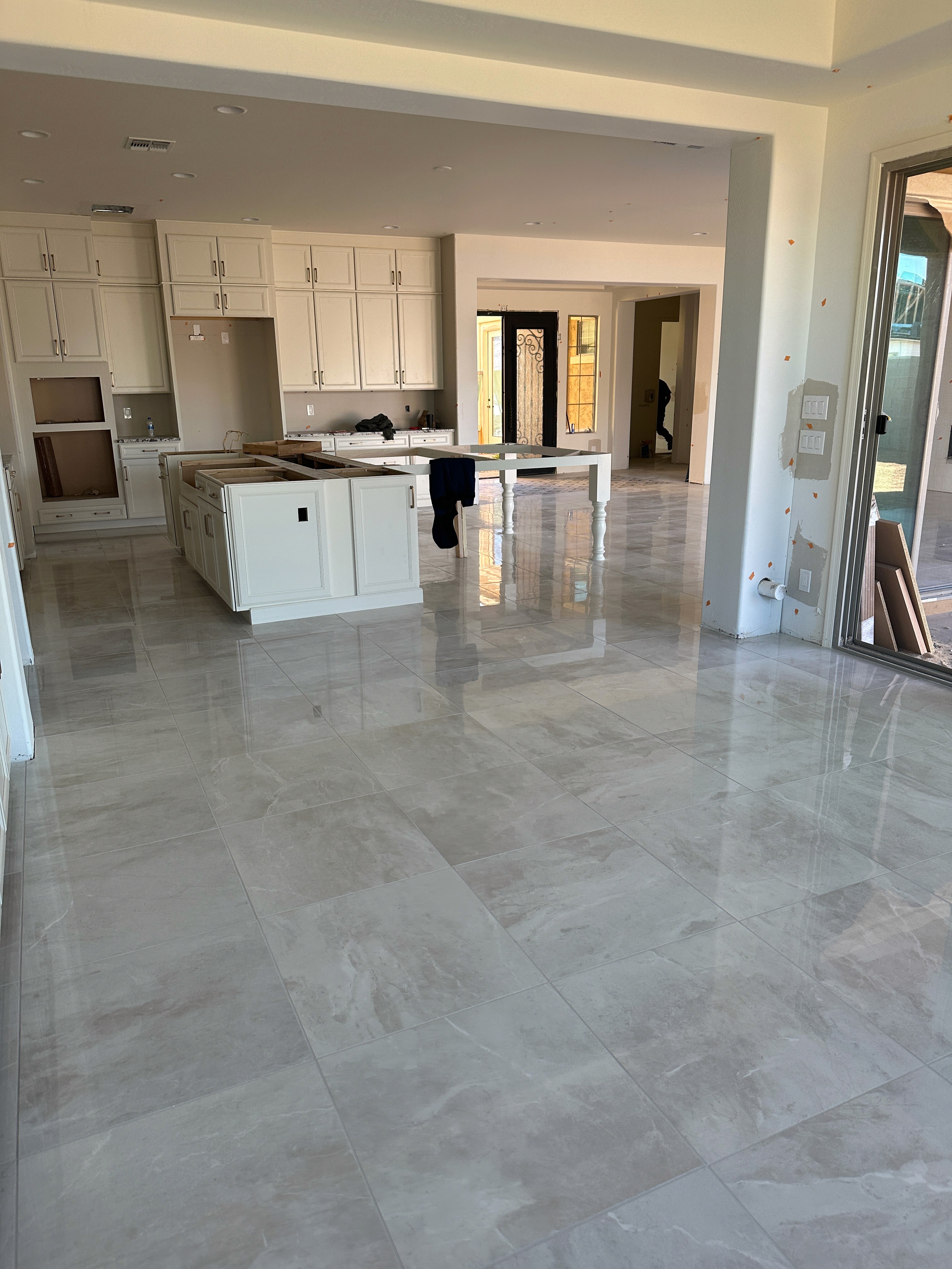 Modern open-plan living area with kitchen island, white cabinets, large sliding glass doors, and glossy marble tiles during construction.