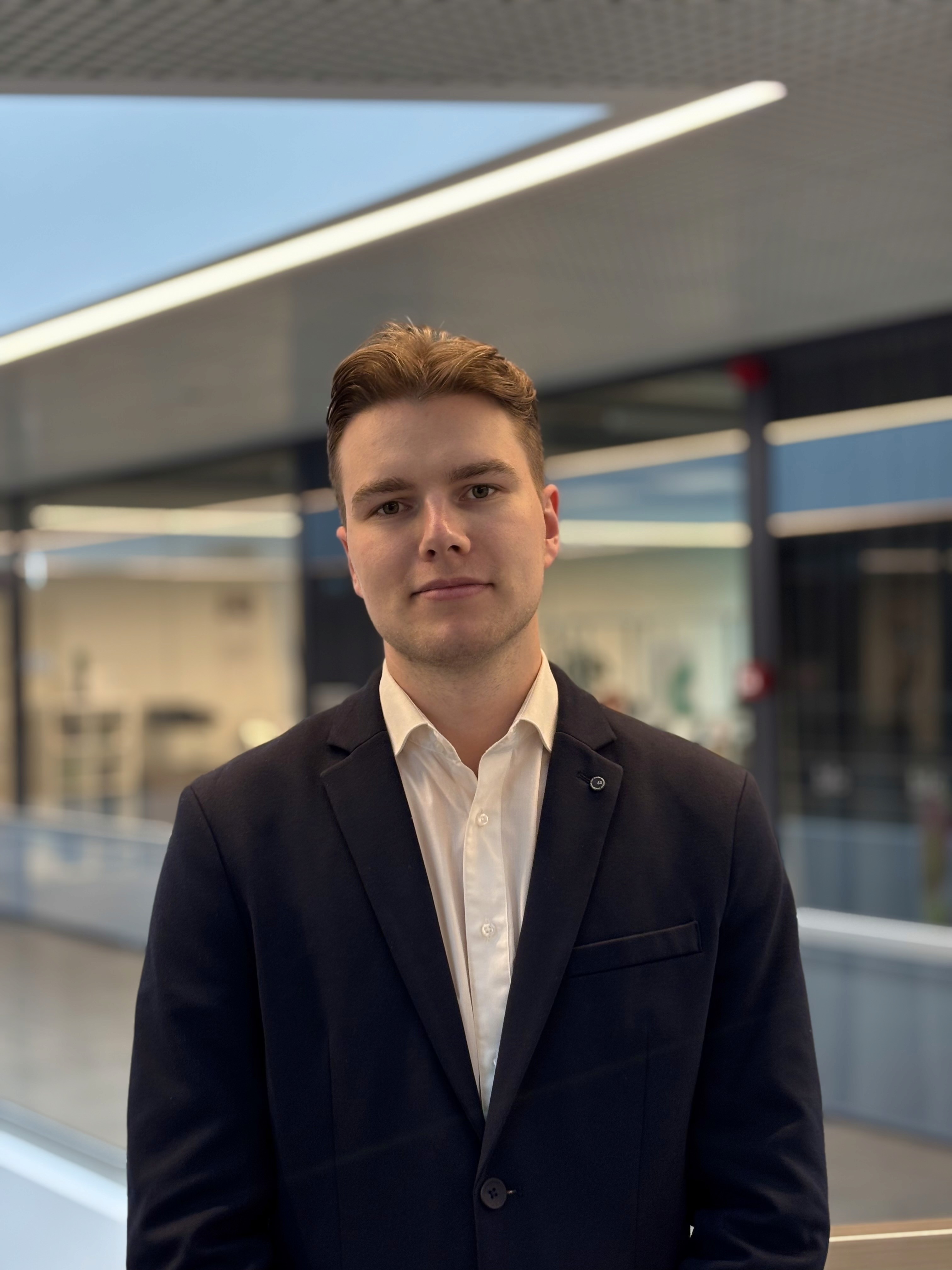 Confident man with short brown hair and beard, wearing a navy zip-up in natural light