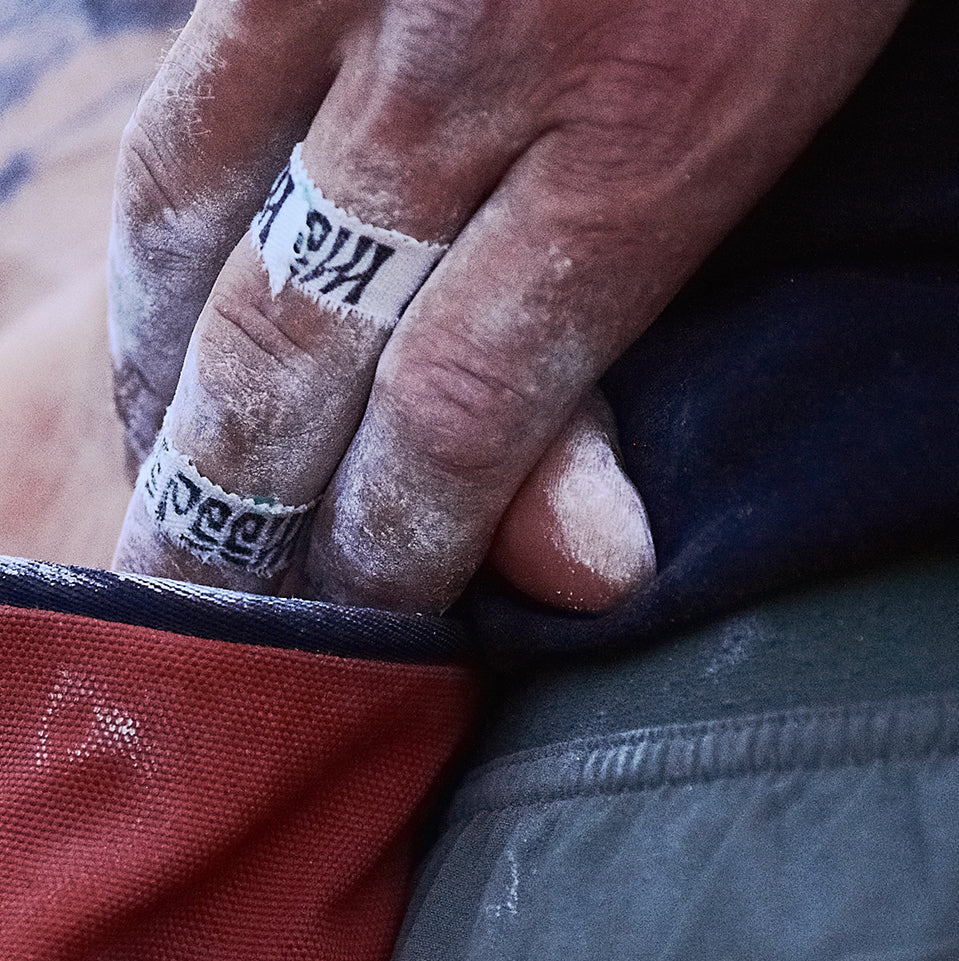 Hand with chalk on fingers gripping a climbing hold, wearing a climbing chalk bag.