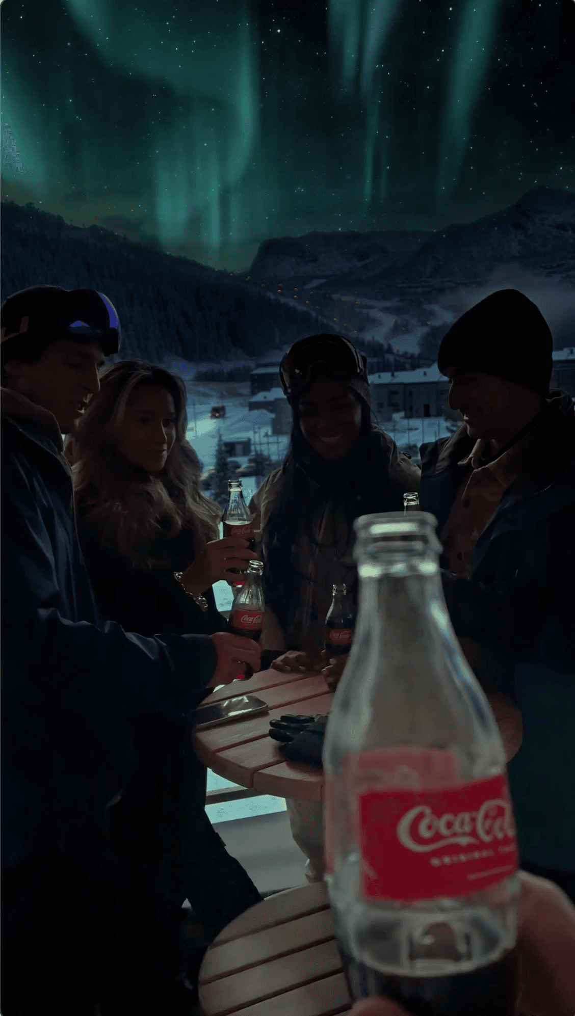 Friends holding Coca-Cola bottles at a snowy night resort