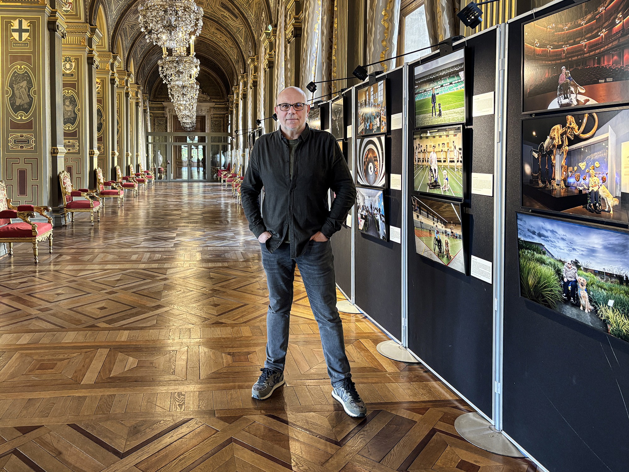 Frédéric Bourcier posé devant ses photographies exposées dans une salle ornée du Palais de la Bourse de Lyon.