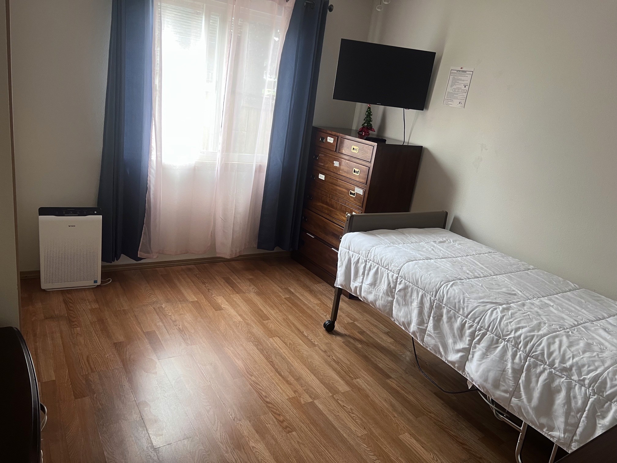 A private resident bedroom with an adjustable bed, dresser, wall-mounted television and a curtained window