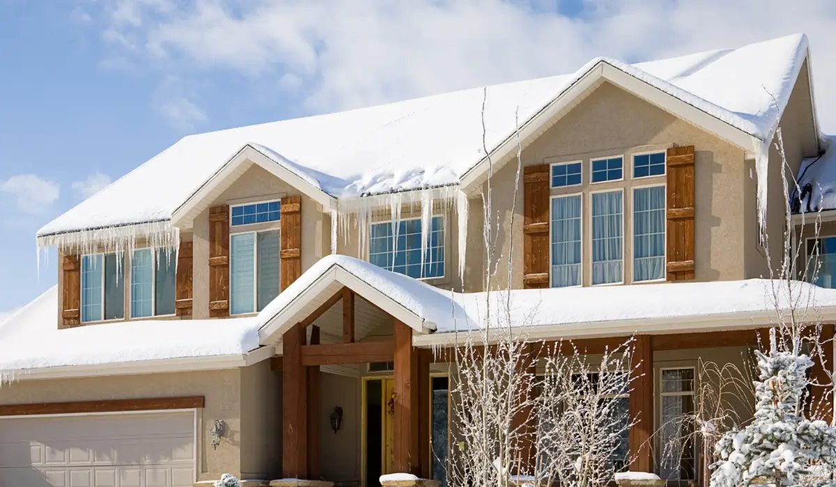 Residential roof showing winter storms damage with ice dams and heavy snow buildup along roof edges.