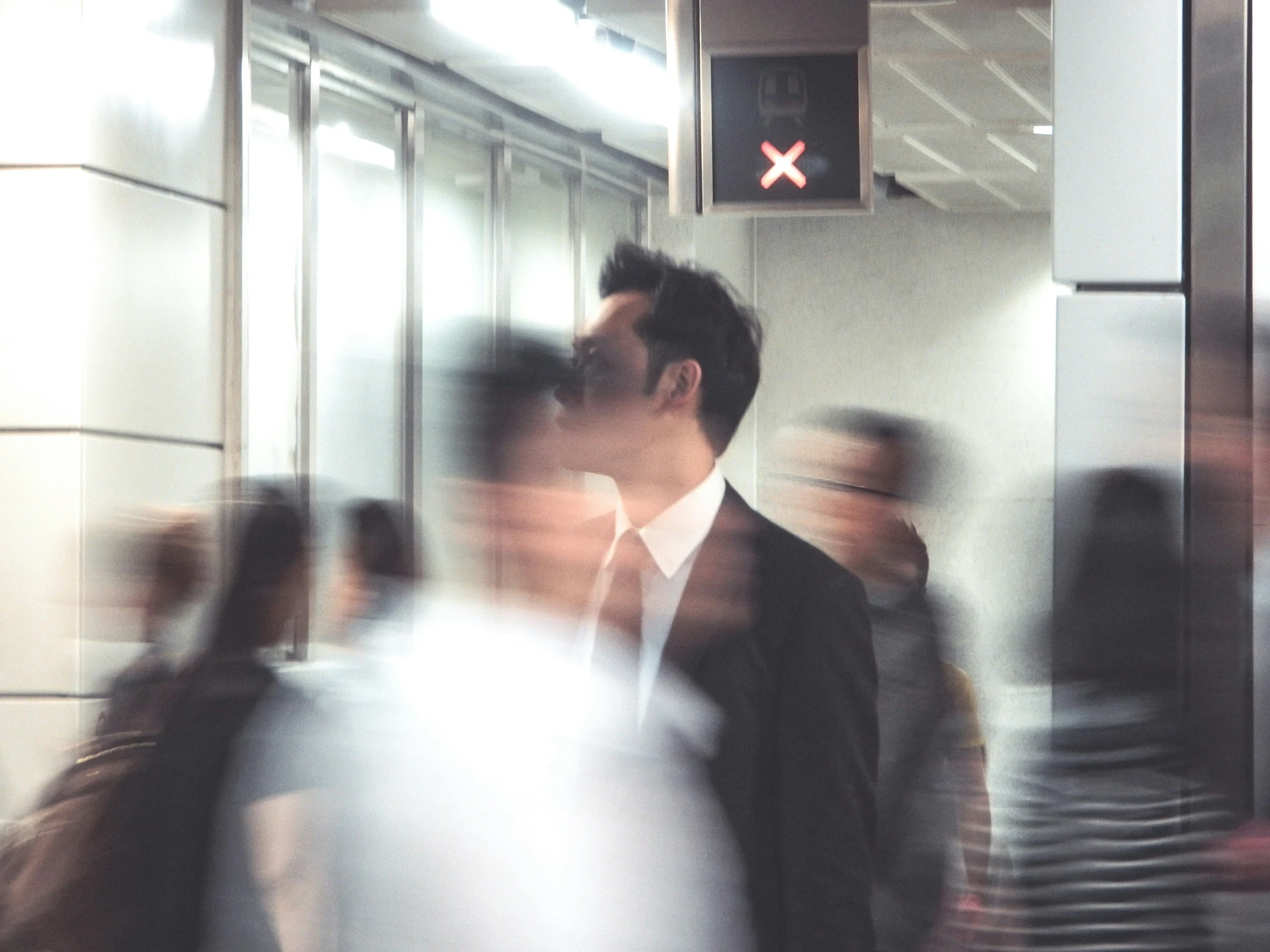 A man in a suit among commuters captured in motion blur at a Hong Kong station.