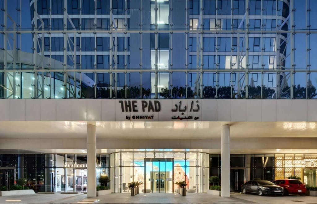 The Pad by OMNIYAT features a large structure with tall glass windows and palm trees in the foreground.