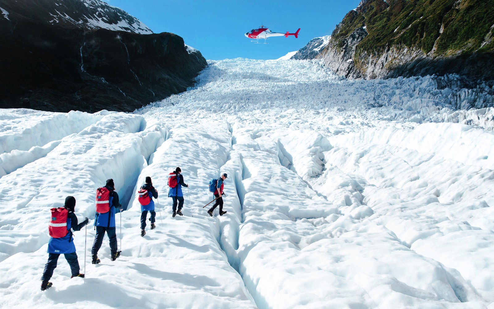 Turistas haciendo senderismo en el Glaciar Fox con un helicóptero sobrevolando, Nueva Zelanda.