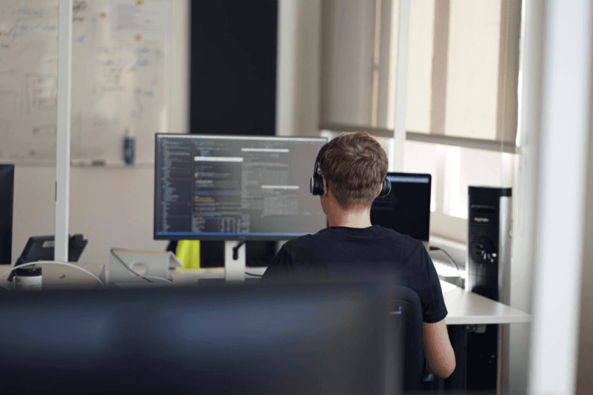 A developer with headphones on working at a desk. There's a whiteboard with notes on it in the background