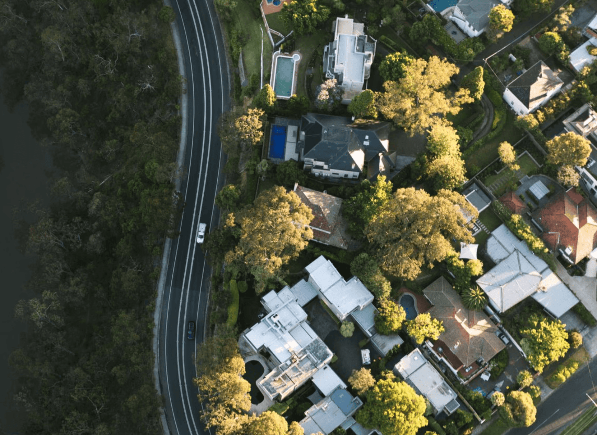 Aerial view of a winding road and affluent homes with pools.