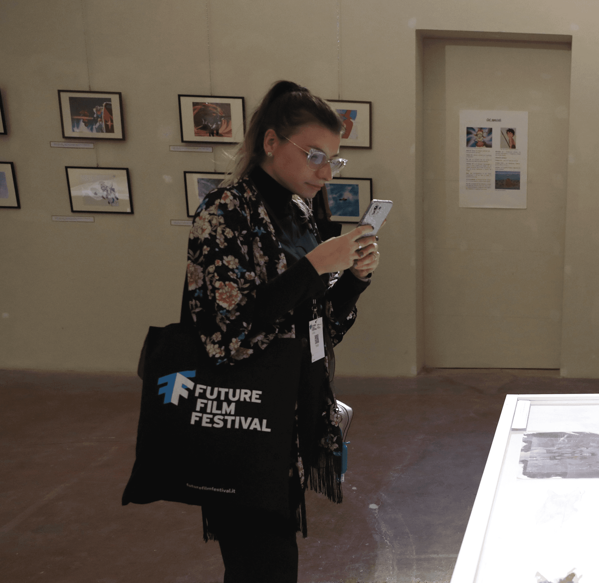 Silvia Vazzana con una shopper del Future Film Festival sulla spalla scatta una fotografia ad un tavolo espositivo con lo smartphone
