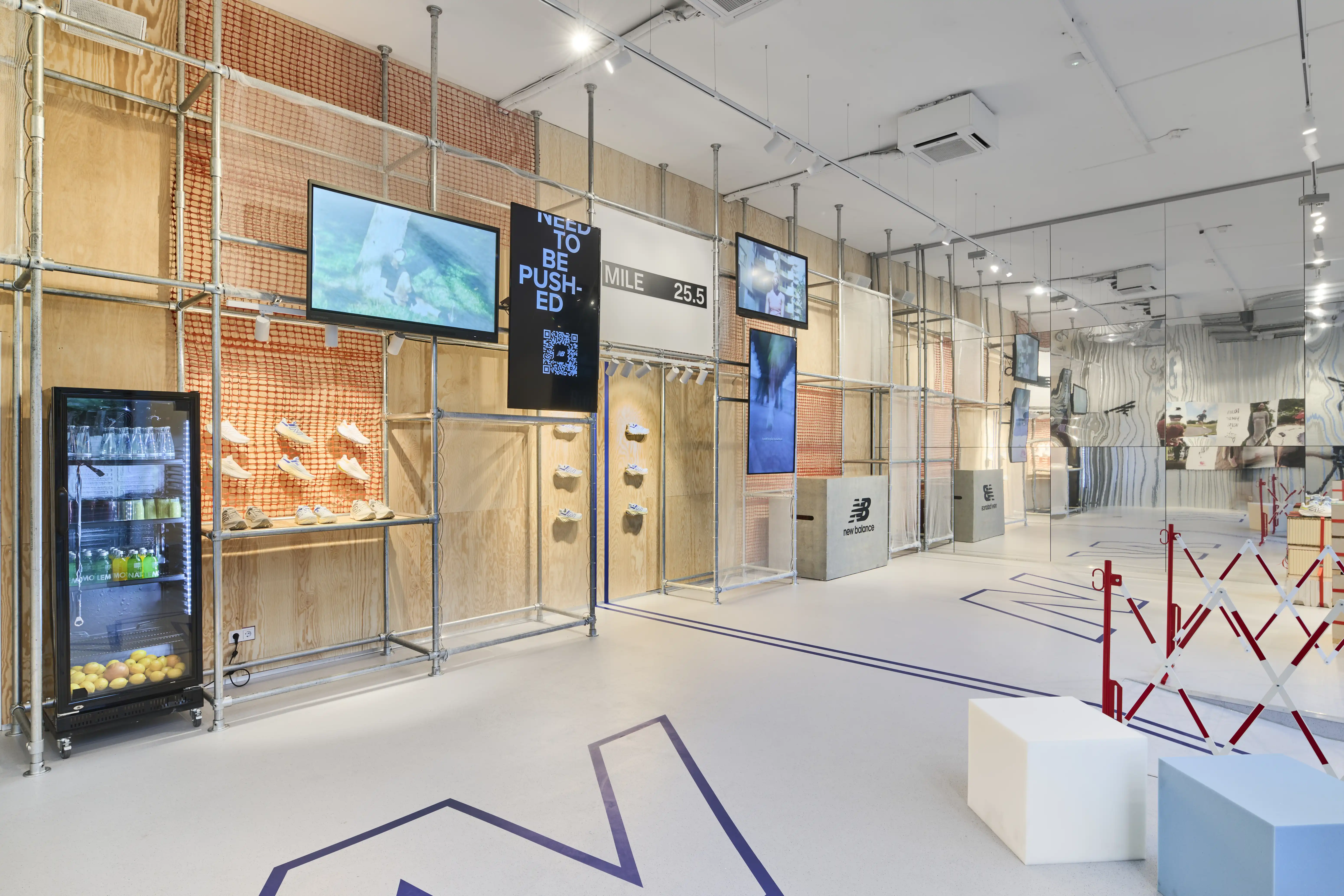 Interior of the Highsnobiety x New Balance pop-up with plywood walls, screens, drinks fridge and marathon-inspired mile markers.