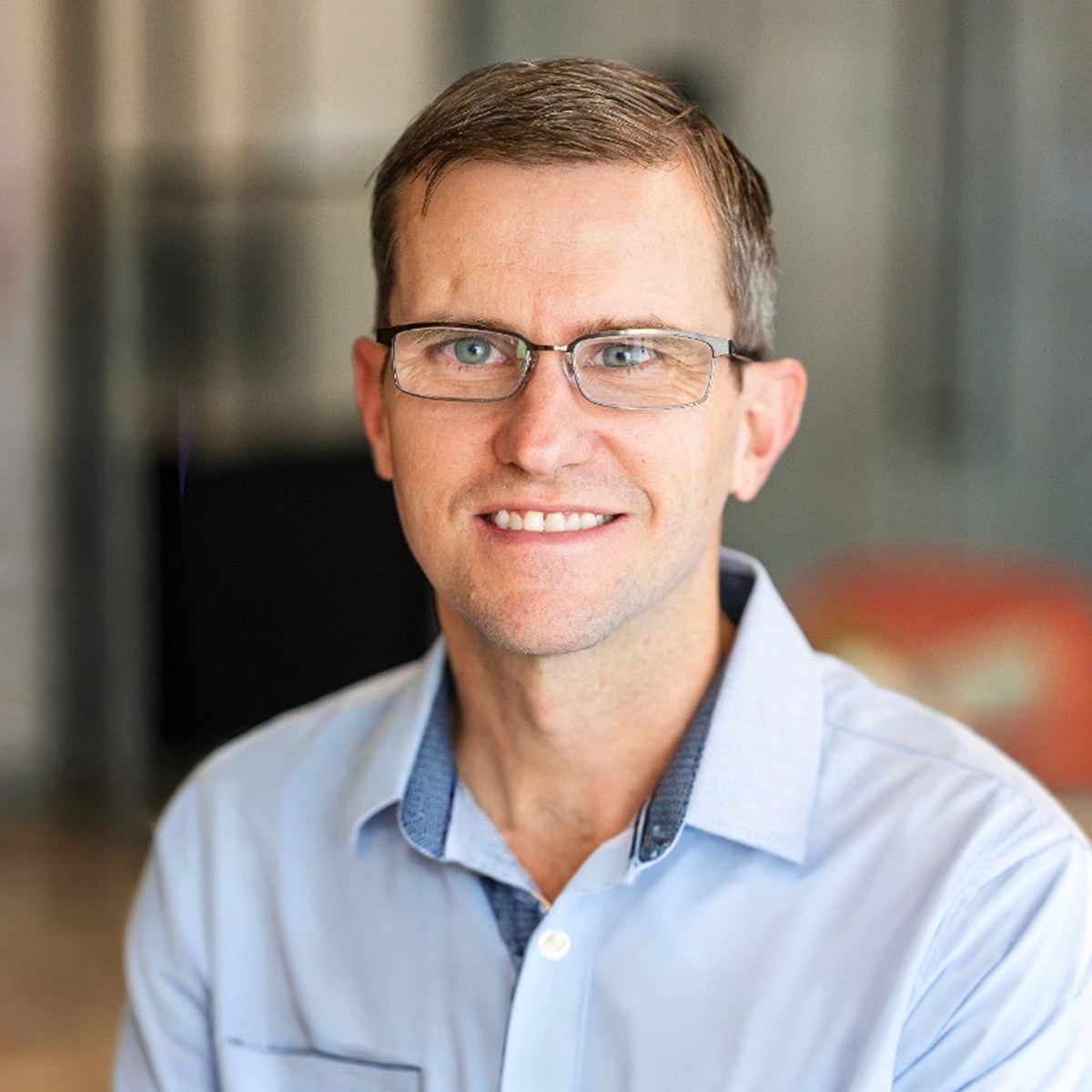 Smiling young man with curly hair, wearing a dark hoodie, against a softly lit background.