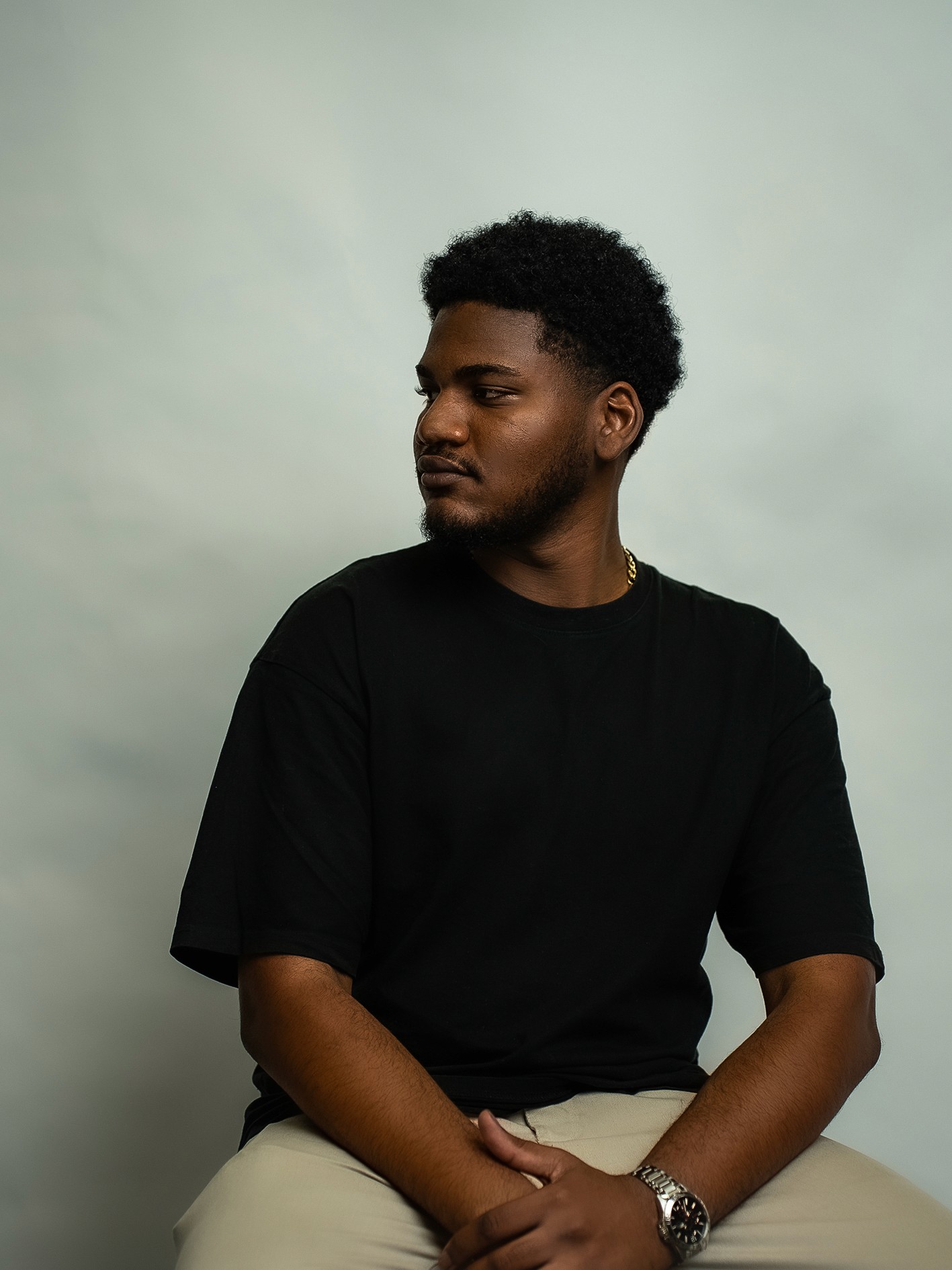 A thoughtful young person with dark hair gazes to the side, captured in soft black and white lighting.