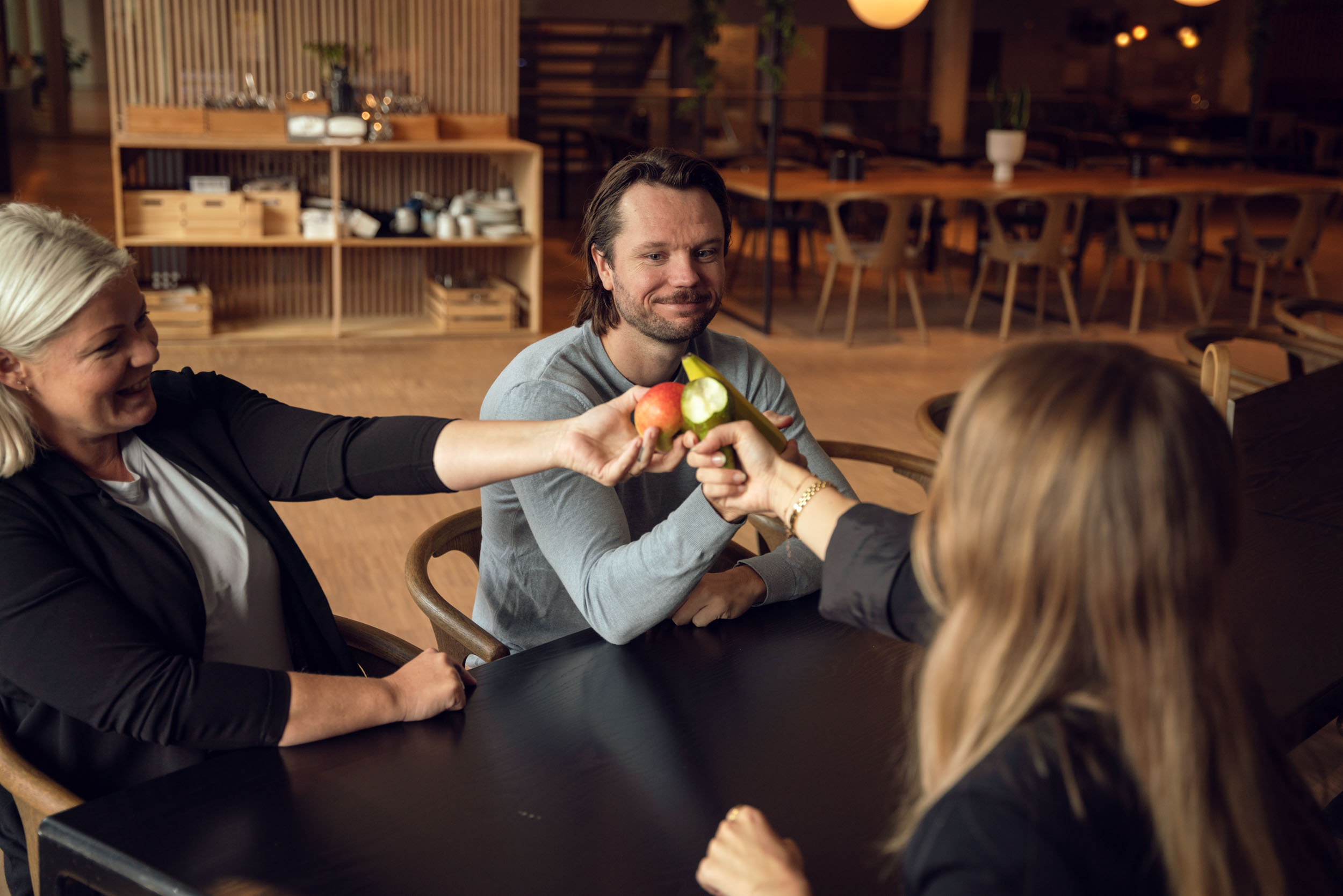 Tre kollegaer sitter rundt et møtebord og tar en fruktpause på arbeidsplassen.