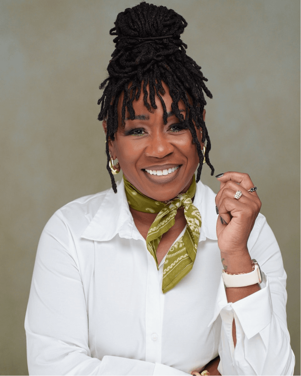 Portrait of Nichelle Hosley, Designer and Founder, smiling while seated and wearing a white blouse and patterned scarf.