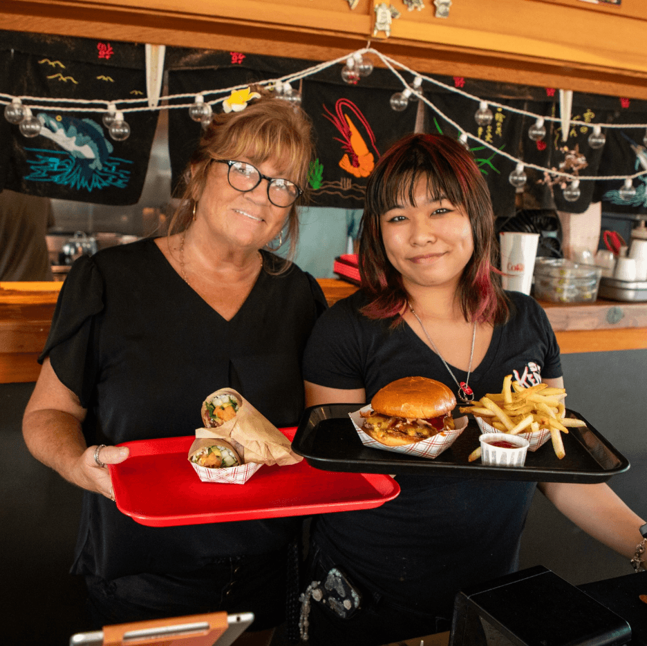 A close-up shot of a fork twirling strands of creamy white pasta, possibly carbonara or cacio e pepe, heavily garnished with dark black pepper or truffle shavings, against a stark white background.