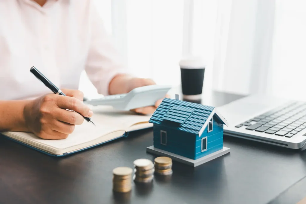 property management software tracking rental finances with a model house, coins, calculator, and laptop on a desk