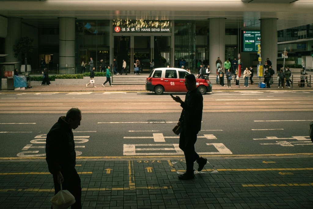 People walk past a red taxi on a city street.