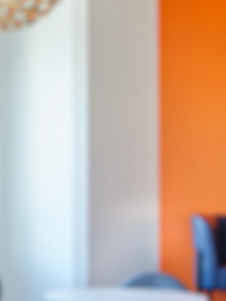 Blurry image of a white wall next to an orange wall. A shelf with small white objects is visible.