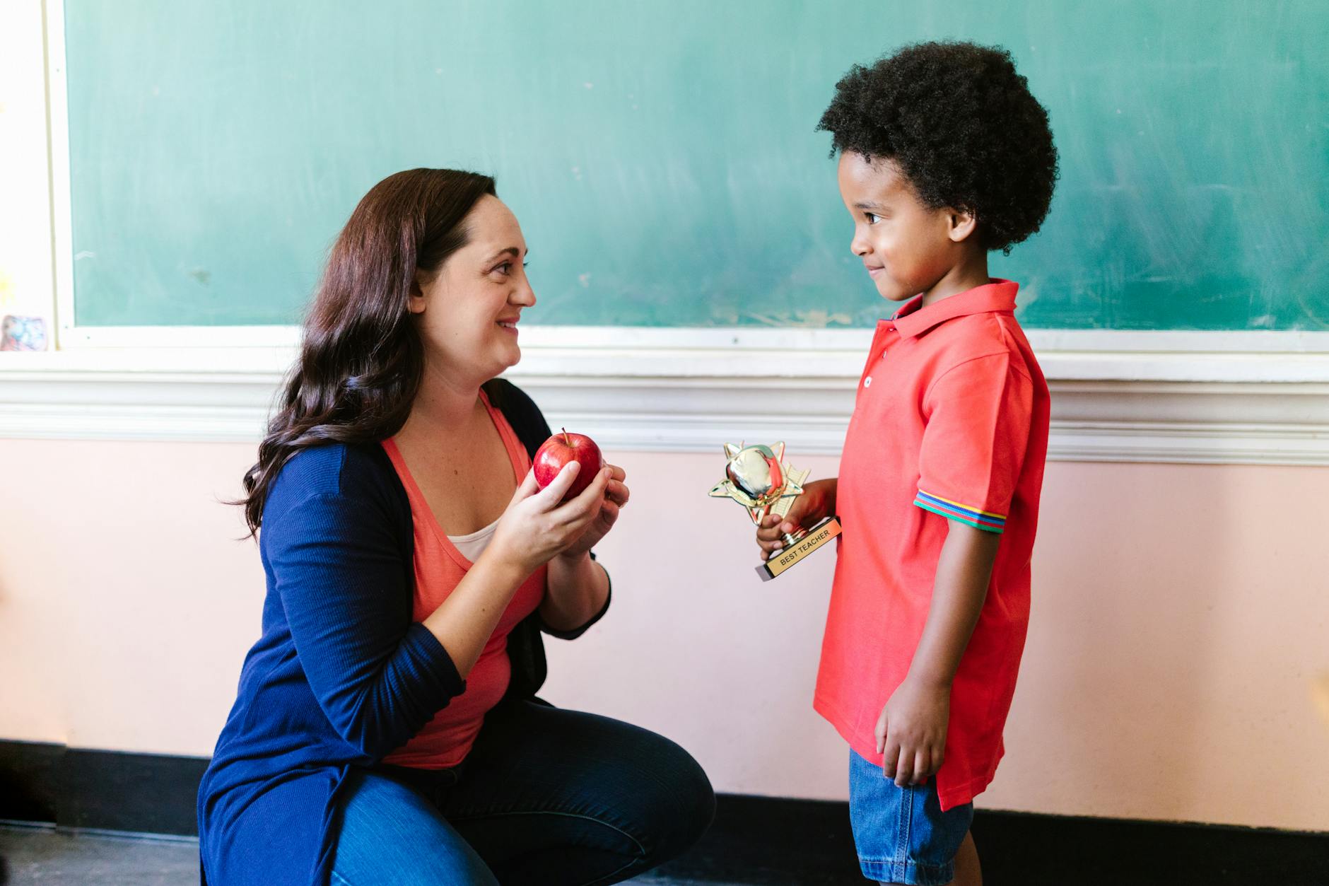 A primary school teacher smiling while sending a message to parents on a smartphone during a classroom break.
