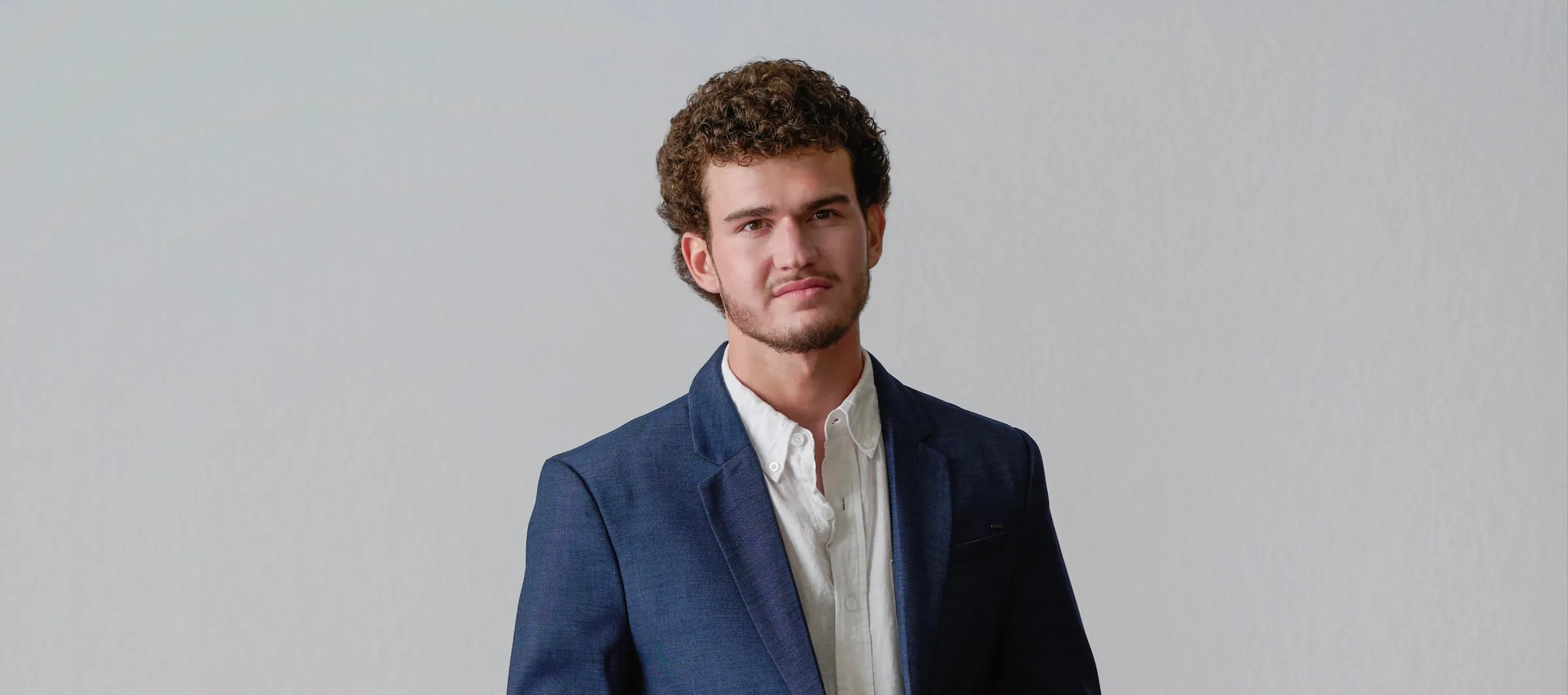 Jeffrey Hakim, a multidisciplinary designer, developer, and ecommerce strategist, standing in a navy blazer against a clean studio background.