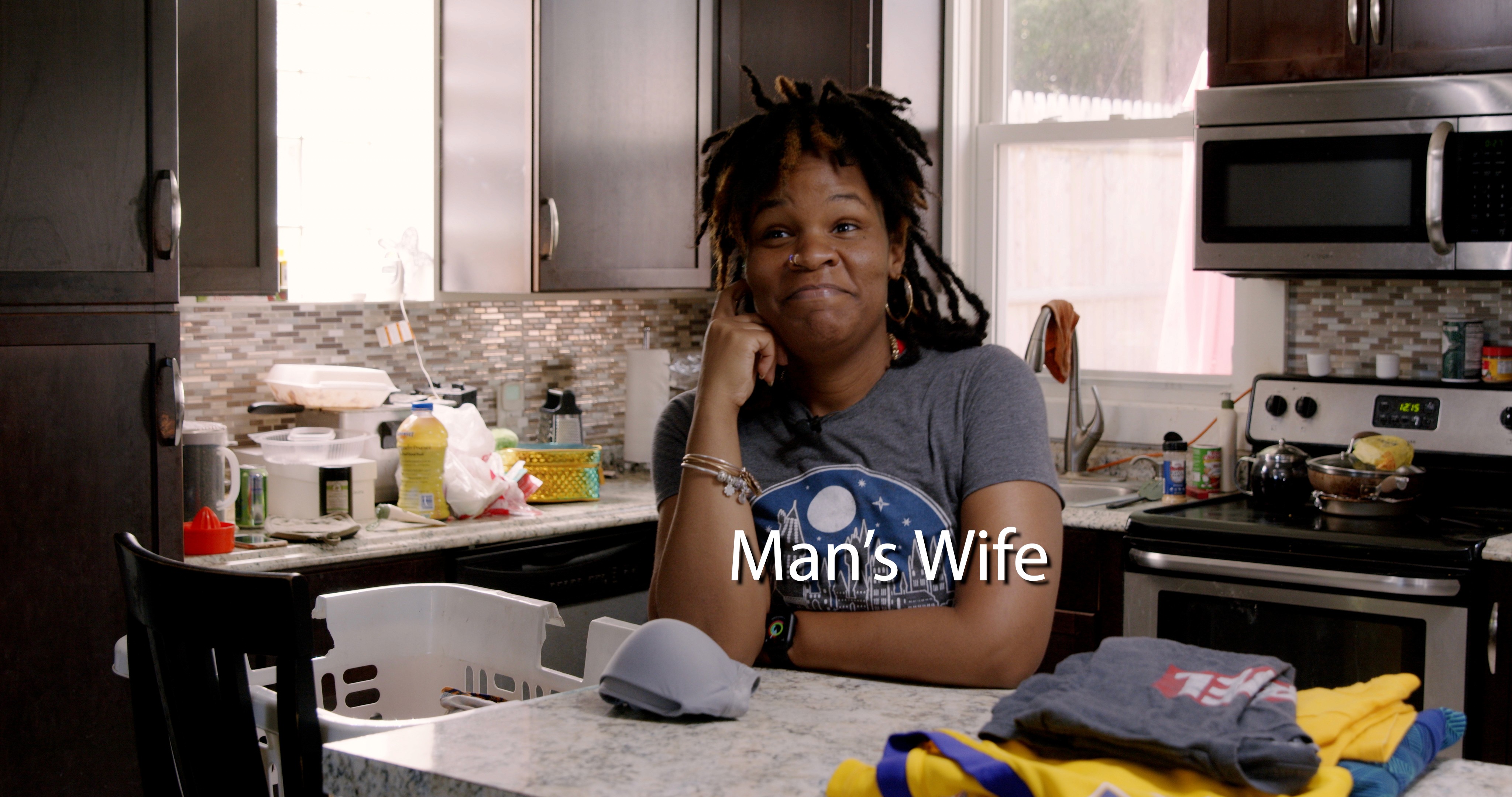 Man's Wife, Asia Davis standing in kitchen smiling mockumentary scene never enough show NeverEnoughShow.com minimocks mockumentary comedy