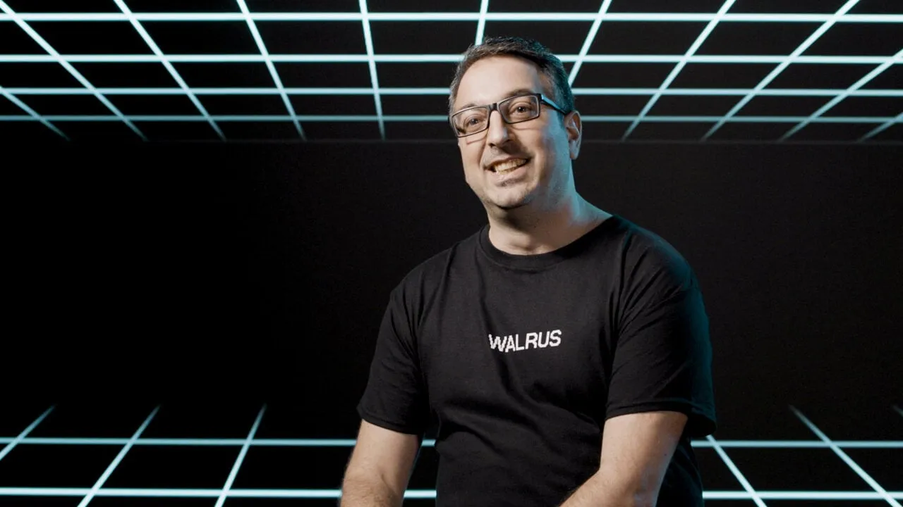 Mysten Labs Chief Scientist George Danezis wearing a "WALRUS" t-shirt in front of a black grid background.