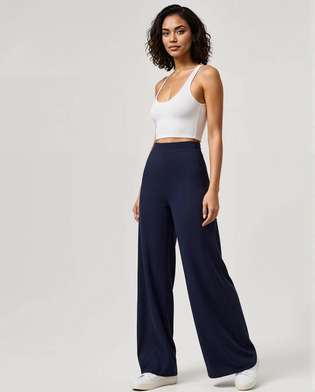 Fashion photograph featuring a white crop top paired with flowing navy wide-leg pants against a minimal light background.