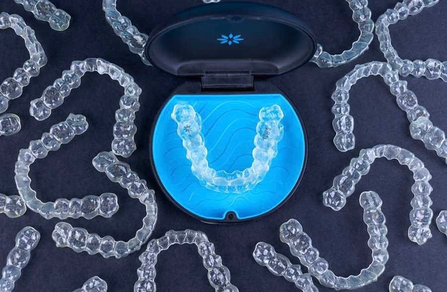 قوالب تقويم الأسنان الشفافة مرتبة بشكل حلزوني مع علبة حفظ سوداء مبطنة بالأزرق بداخلها قالب واحد، تعرض حلول تجميل الأسنان الحديثة والمبتكرة للحصول على ابتسامة مثالية بطريقة غير مرئية