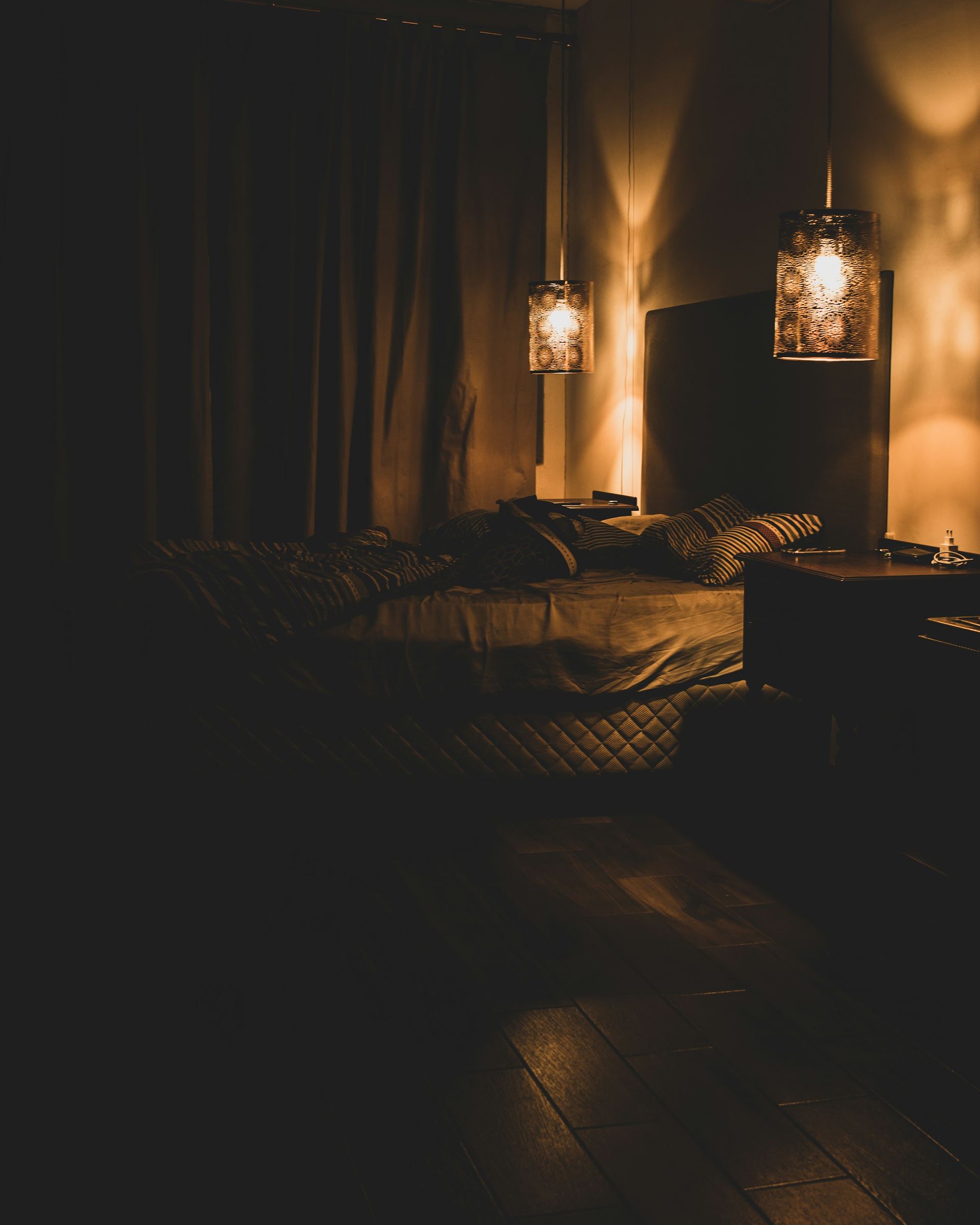 Pendant lamps glowing over a bed in a dark, quiet room